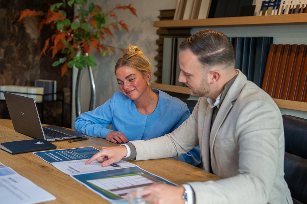 Twee personen in gesprek aan een tafel terwijl zij documenten en plattegronden bekijken en de mogelijkheden en kansen bespreken van beleggen in een bedrijfspand in Gouda, met laptop en vastgoedinformatie zichtbaar op tafel