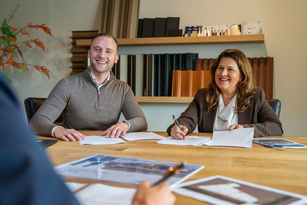 Beleggen in een bedrijfspand in Heinenoord wordt tijdens een persoonlijk gesprek aan tafel, door twee adviseurs doorgenomen. Ze ondertekenen documenten in een kantooromgeving met materiaalstalen en plannen op tafel.