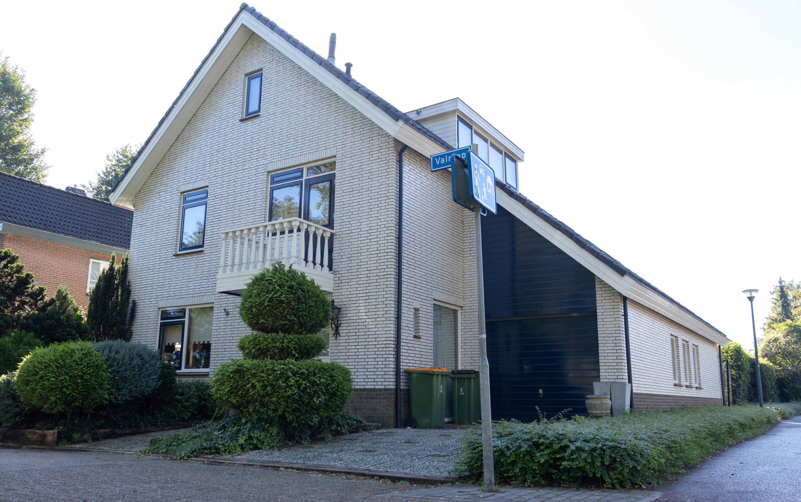 Huis te koop aan de Valreep in Veenendaal, met een lichte bakstenen gevel, wit balkon, groene voortuin en oprit naast de woning.