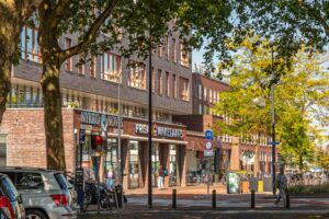 Straatbeeld in Enschede met zicht op een modern appartementencomplex en winkels op de begane grond. Ideaal voor wie op zoek is naar een woning in Enschede om te kopen.