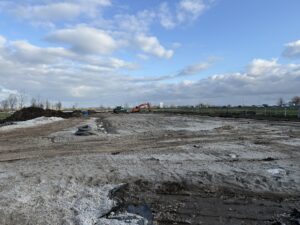 Grondwerkzaamheden in voorbereiding op de bouw van het nieuw bedrijfspand in Bodegraven, met zicht op de A12 en bouwmaterieel op de achtergrond onder een uitgestrekte wolkenlucht.