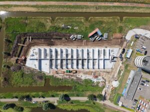 Luchtfoto van de bouw van een nieuw bedrijfspand in Bodegraven met zicht op fundering, betonnen wanden en omliggende bedrijvigheid aan het water.
